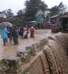 People standing on a flooded road in Myanmar next to a house that washed away.