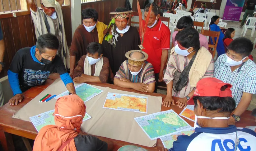 Indigenous community members evaluate maps while sitting at a table in Peru in June 2022
