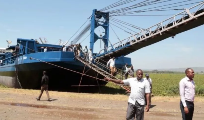 men in Africa standing in front of a barge with a bridge in the background
