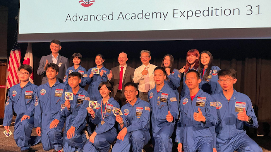 Group photo with Dan Irwin, Tony Kim, Krit Kunplin, and the recipients, on stage at Space Camp graduation ceremony SERVIR'S Dan Irwin and Tony Kim (back center) and Zignature CEO and education advocate Krit Kunplin (back left)  take the stage to pose with the recipients of the Discover Thailand's Astronauts Scholarship at their  Space Camp graduation on April 28.  (Photo credit: Dan Irwin, NASA)