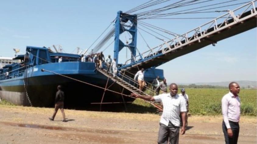 men in Africa standing in front of a barge with a bridge in the background